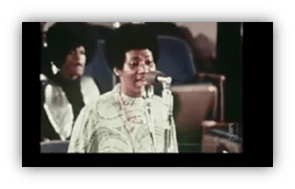 "Live performance featuring a singer with an Afro hairstyle at a microphone."