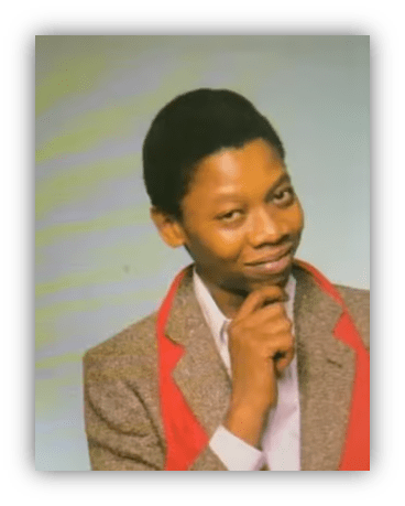Young man in a blazer with a red collar, smiling thoughtfully against a light background.