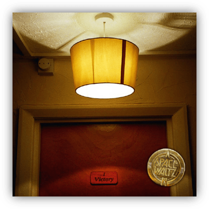 "Vintage ceiling lamp illuminating a door labeled 'Victory' with a round emblem."