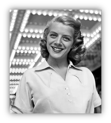 Smiling young woman in vintage attire, illuminated by bright marquee lights.