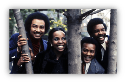 "Four smiling musicians posing playfully behind a tree."