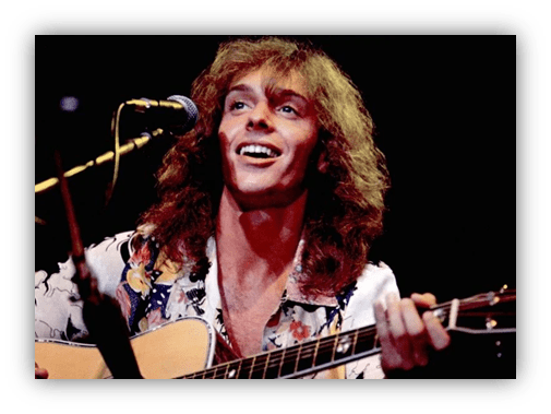 "Smiling musician with long hair playing guitar on stage."