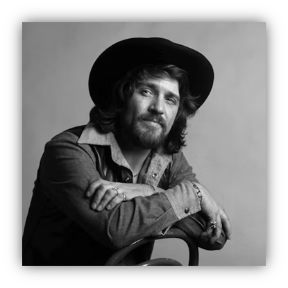 Black and white portrait of a man with long hair and a hat, sitting casually on a chair.