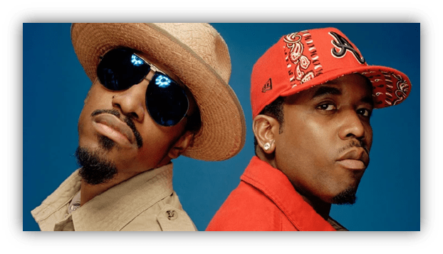 Two male hip-hop artists posing back-to-back, wearing stylish hats and sunglasses against a blue background.