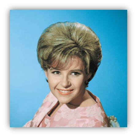 Smiling woman with voluminous hair, wearing a pink blouse, against a blue background.