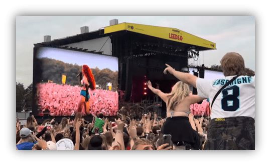 Crowd enjoying a live concert with a performer on stage and a large screen displaying the show.