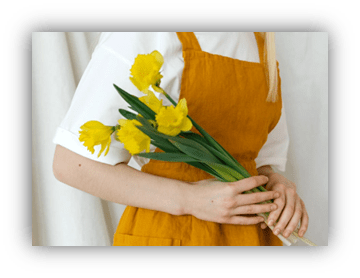 "Person in a yellow apron holding a bouquet of yellow daffodils."