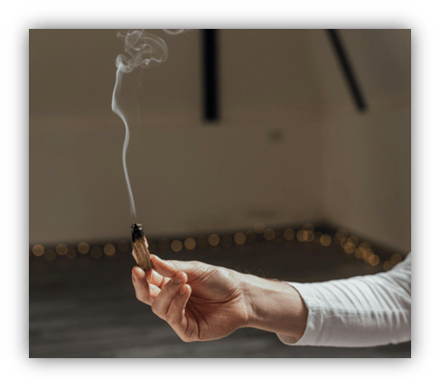 "Hand holding a burning sage stick with smoke in a cozy room."