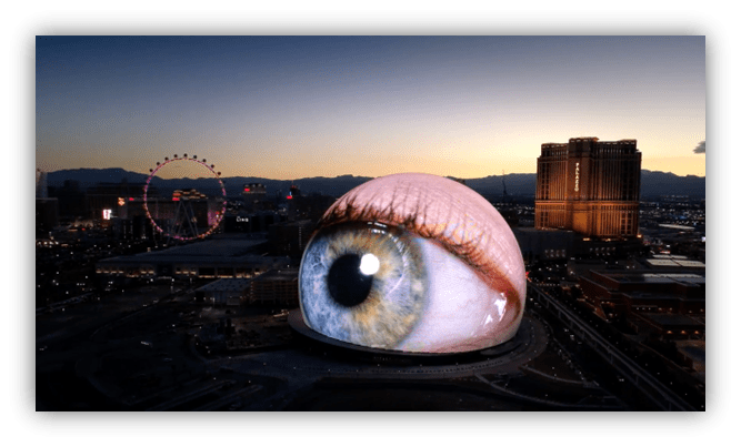 Giant eye display on building in Las Vegas at sunset, with Ferris wheel in background.