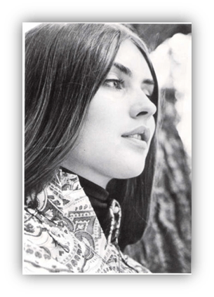 Black and white portrait of a woman with long hair, wearing a patterned jacket, gazing thoughtfully outdoors.