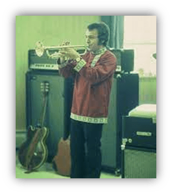 "Man playing trumpet in a vintage music studio with guitars and amplifiers."