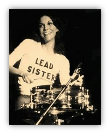"Female drummer wearing 'LEAD SISTER' shirt, smiling while performing."