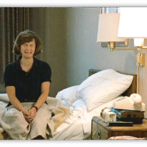 Woman sitting on a bed in a hotel room, expressing a mix of emotions.
