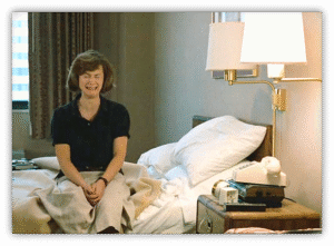 Woman sitting on a bed in a hotel room, expressing a mix of emotions.