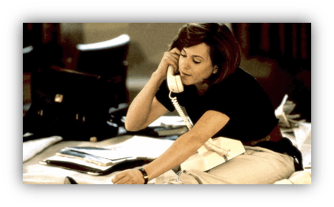 Woman talking on a telephone while sitting among papers and office supplies.