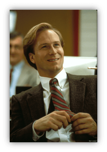 Smiling man in a suit, seated in an office setting, exuding confidence and professionalism.