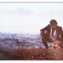 Man crouching on a hillside with a cityscape in the background.