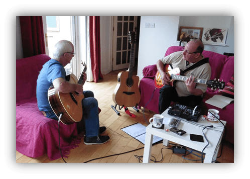 Two men playing guitars in a cozy living room.
