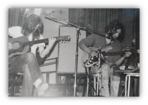"Two musicians performing live, one on acoustic guitar and the other on electric guitar, in a vintage setting."