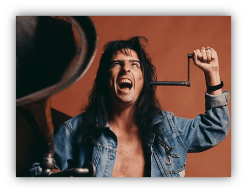"Man with long hair and denim jacket making a dramatic expression while holding a crank."