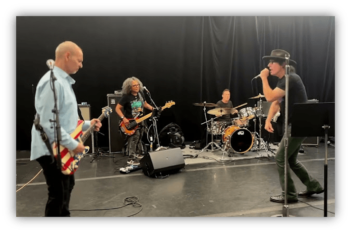 Band rehearsing on stage with guitars and drums.