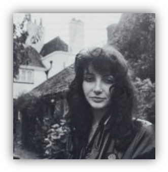 "Black and white portrait of a woman with curly hair in front of a cottage."