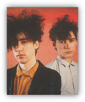 "Two musicians with curly hair posing against a red background."