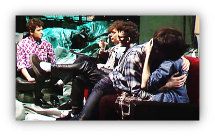"Group of friends sitting in a casual setting, two are embracing while others engage in conversation."