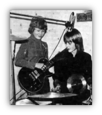 "Two young musicians in a studio, one playing guitar and the other on drums."