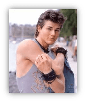 "Young man posing by the water, wearing a sleeveless shirt and bracelets."