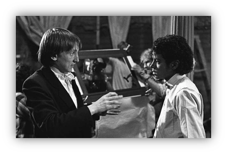 "Black and white image of a director discussing a scene with a young actor on set."