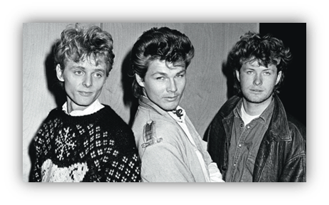 "Black and white photo of three musicians in 1980s fashion."