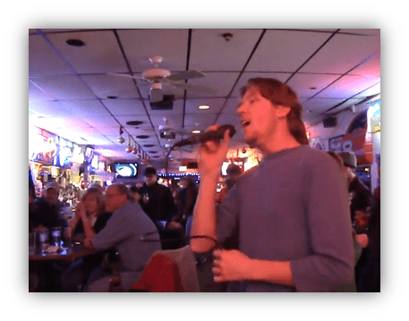 "Man singing karaoke in a lively bar with an engaged audience."