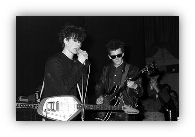 "Black and white photo of two musicians performing on stage, one singing with a microphone and the other playing guitar."