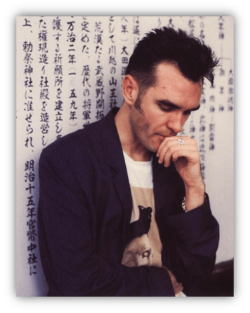 "Man in a striped jacket with a contemplative expression, standing against a wall covered in Japanese text."