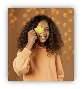 "Smiling girl holding a yellow leaf against a fall-themed background."