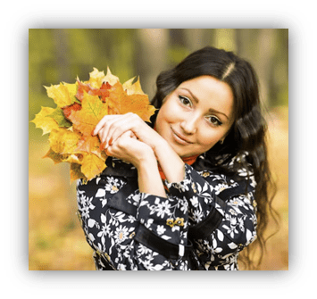 Young woman holding vibrant autumn leaves in a forest setting.