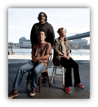 Three people posing on chairs by the waterfront, with a city skyline and bridge in the background.