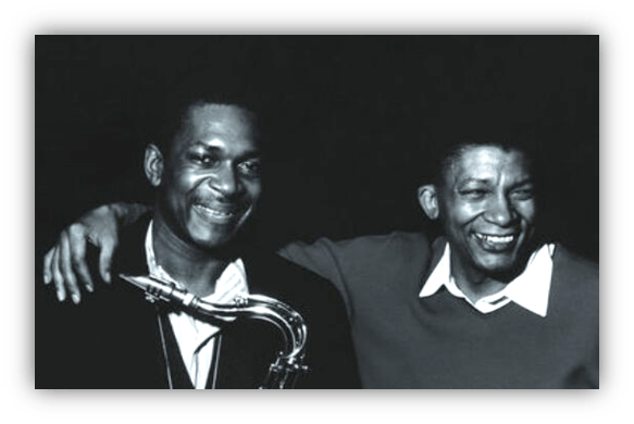 "Black and white photo of two musicians smiling, one holding a saxophone."