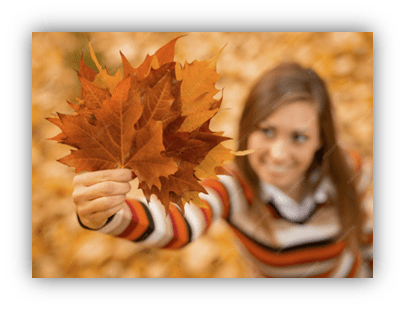 "Smiling woman holding vibrant autumn leaves in a colorful sweater."
