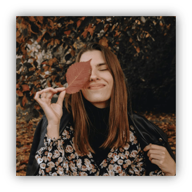 Young woman smiling with a leaf in autumn foliage.