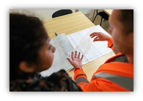 "Two professionals discussing plans over a blueprint at a table."