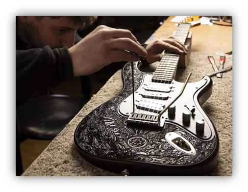 "Close-up of a person adjusting the strings on an intricately designed electric guitar in a workshop."