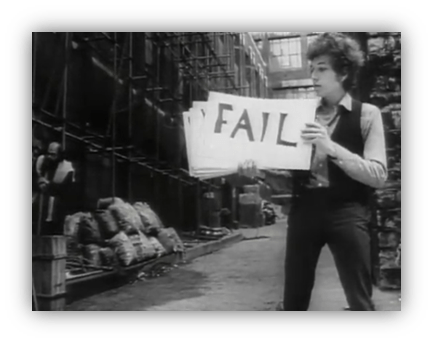 "Black and white image of a young man holding a sign that reads 'FAIL' in an urban setting."