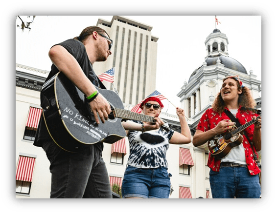"Three musicians performing with guitars at a rally, celebrating freedom and unity, with American flags in the background."