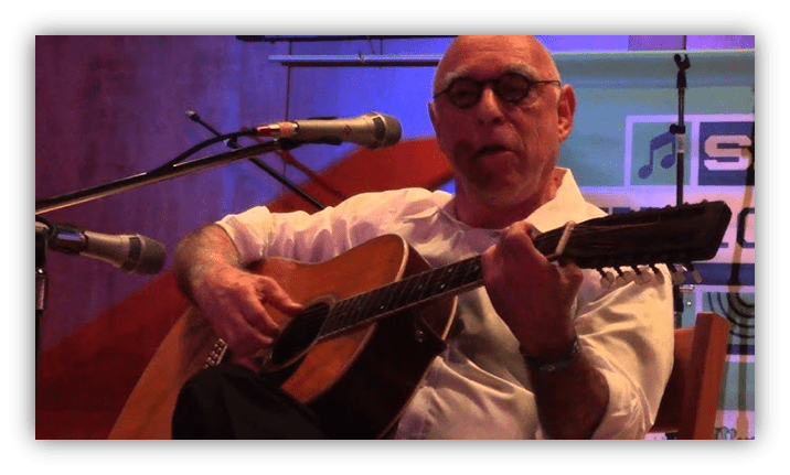 Musician playing acoustic guitar on stage, focused expression.