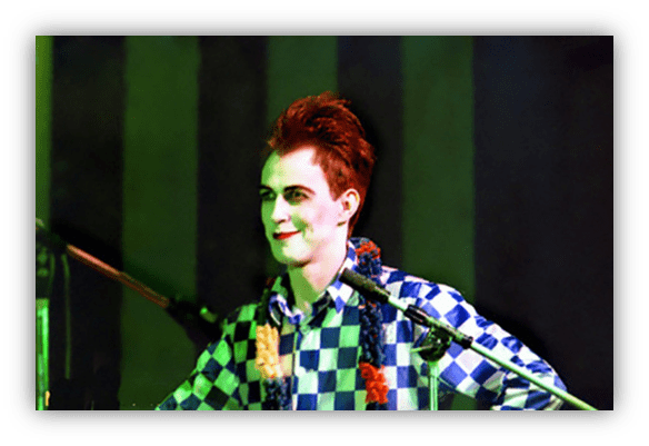 "Male performer with vibrant hair and checkered shirt on stage."