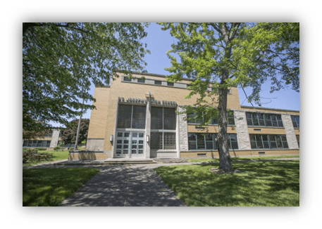 "Front view of a modern educational building surrounded by green trees and grass."