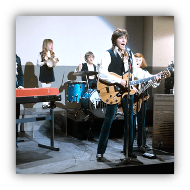 "1960s band performing on stage with instruments and vocals."