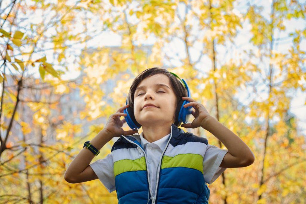 Boy enjoying music with headphones in a colorful autumn setting.